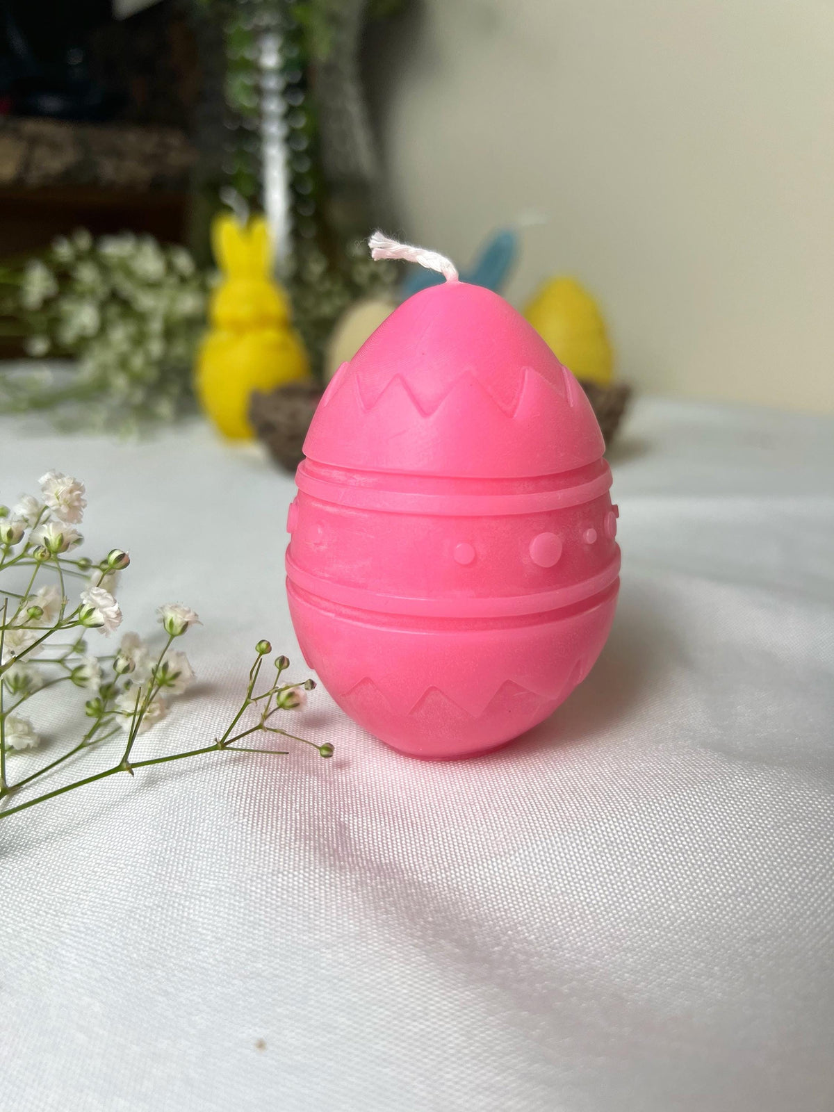 Pink handmade egg-shaped candle on a white fabric with spring flowers and Easter decorations