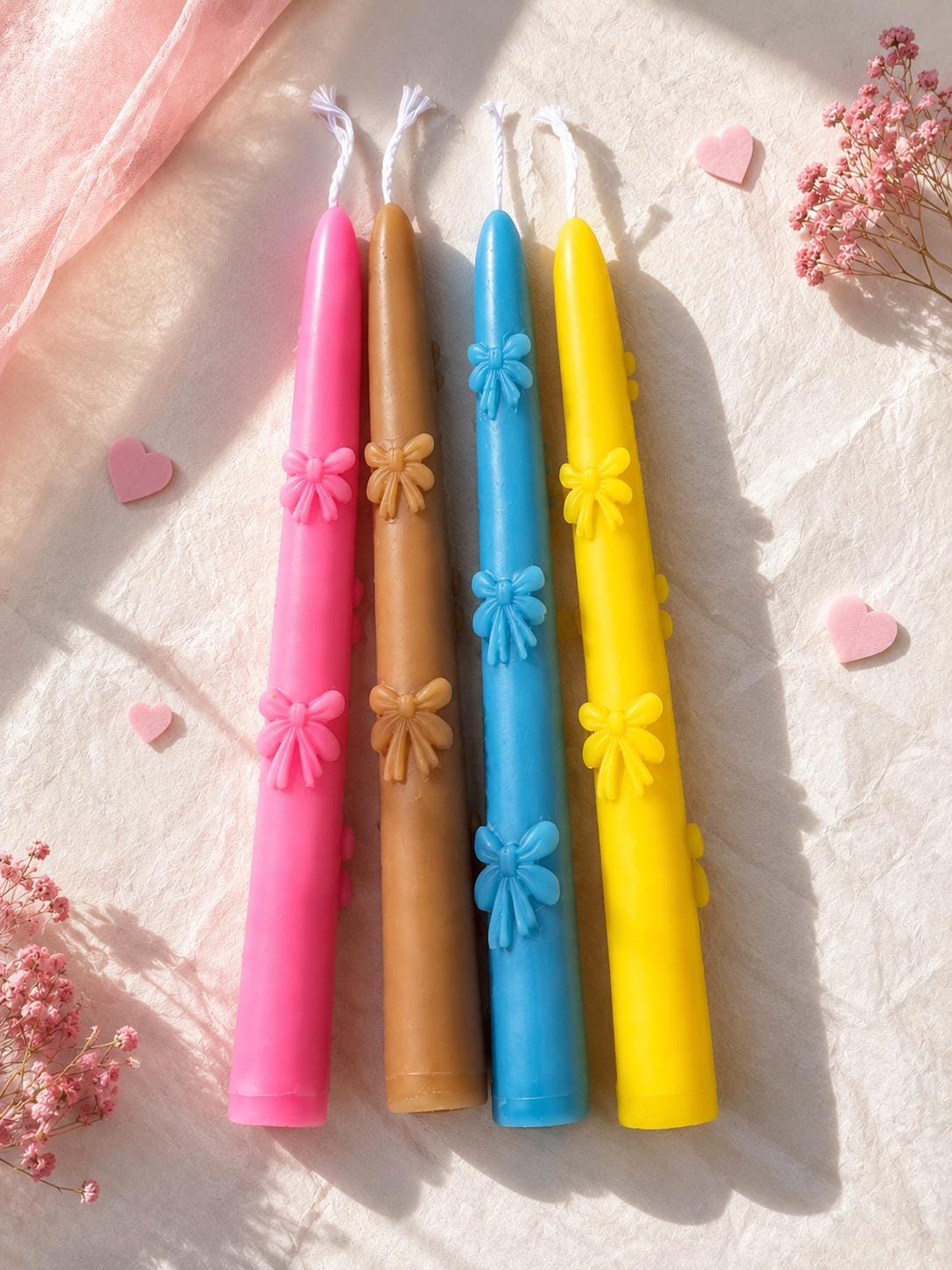 Set of four handmade colorful taper candles with floral details on a soft neutral fabric