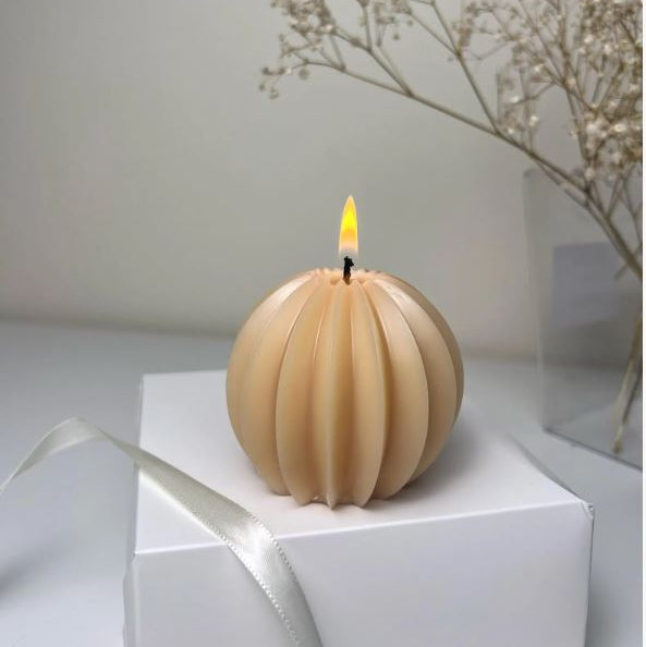 Lit handmade beige sphere candle displayed on a white gift box with a satin ribbon, creating a warm and cozy minimalist home decor scene.