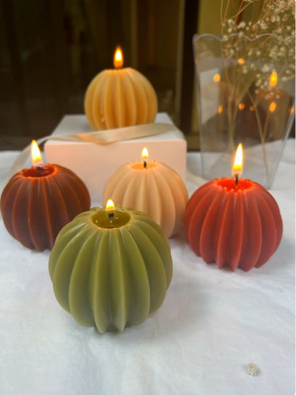 Handmade ribbed sphere candles in green, orange, brown, and cream with lit wicks on a decorative table
