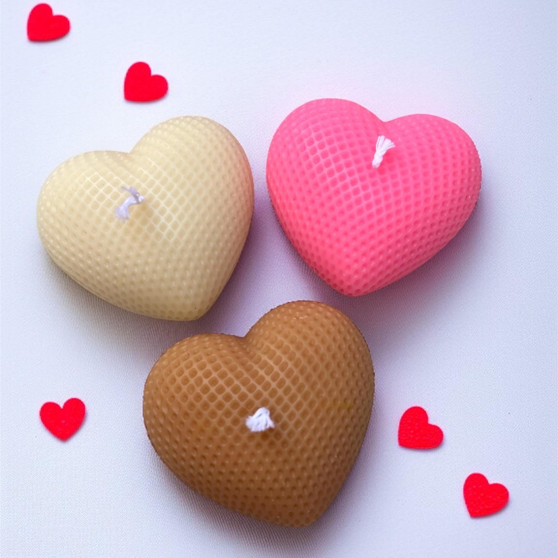 Three heart-shaped beeswax candles in beige, pink, and brown, arranged on a white background with small red heart cutouts.